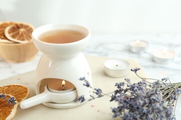 Aroma lamp with burning candle, lavender and dry orange slices on white table, closeup
