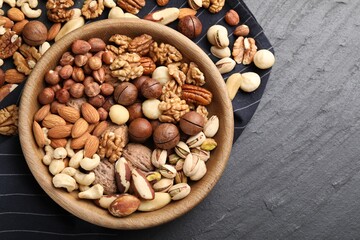 Mix of different nuts in bowl on black table, top view. Space for text