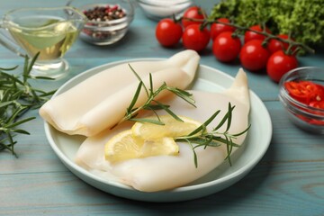 Uncooked squids with lemon slices, rosemary and spices on blue wooden table, closeup