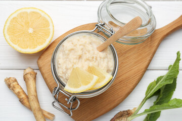 Tasty horseradish sauce with lemon slices and roots on white wooden table, flat lay