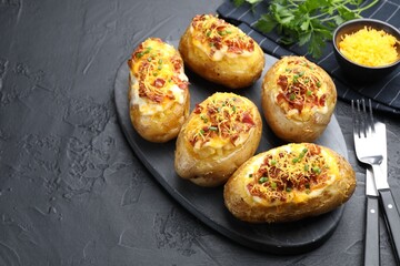 Tasty stuffed baked potatoes served on black textured table, closeup. Space for text