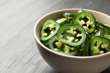 Pieces of green jalapeno peppers in bowl on grey table, closeup. Space for text