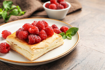 Yummy puff pastry with raspberries on wooden table, closeup