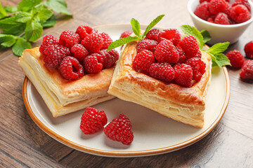 Yummy puff pastries with raspberries and mint on wooden table, closeup