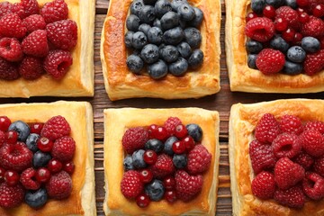 Tasty puff pastries with berries on wooden table, flat lay