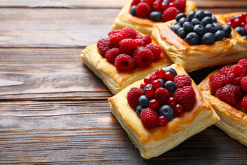 Tasty puff pastries with berries on wooden table, closeup. Space for text