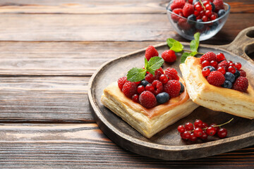 Tasty puff pastries with berries and mint on wooden table, closeup. Space for text