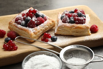 Tasty puff pastries with berries and powdered sugar on grey table, closeup