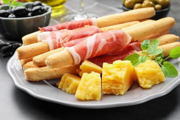 Grissini breadsticks with prosciutto and cheese on grey table, closeup