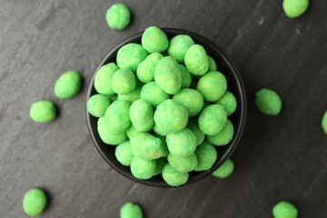 Delicious wasabi coated peanuts and bowl on dark textured table, flat lay