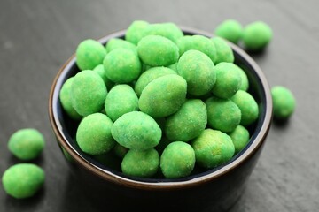 Delicious wasabi coated peanuts and bowl on dark textured table, closeup