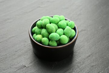 Delicious wasabi coated peanuts in bowl on dark textured table, closeup