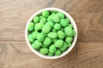Delicious wasabi coated peanuts in bowl on wooden table, top view