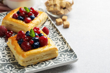 Tasty puff pastries with berries, mint and brown sugar on light grey table, closeup. Space for text
