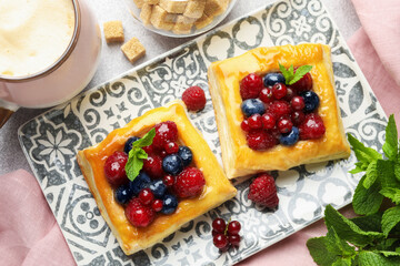Tasty puff pastries with berries, mint, brown sugar and coffee on light grey table, flat lay