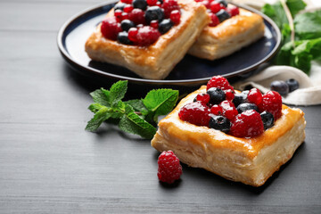 Tasty puff pastries with berries and mint on grey wooden table, closeup. Space for text