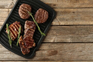 Delicious grilled beef meat with rosemary on wooden table, top view. Space for text