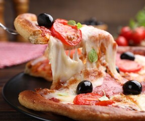 Taking piece of delicious pizza with cheese, salami, tomatoes and olives at table, closeup