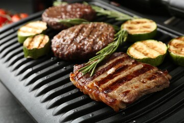 Electric grill with beef steaks, zucchini and rosemary on black table, closeup