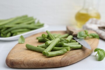 Cut green bean pods and knife on white table, closeup