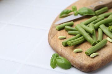 Cut green bean pods and knife on white tiled table, closeup. Space for text