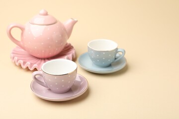Beautiful ceramic tea set for children on beige background, closeup. Space for text