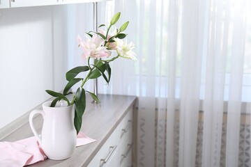 Beautiful lily flowers in jug on wooden cabinet indoors, space for text