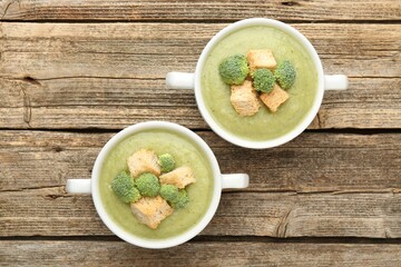 Tasty broccoli cream soup with croutons in bowls on wooden table, flat lay