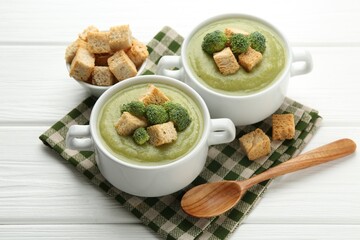 Tasty broccoli cream soup with croutons served on white wooden table, closeup