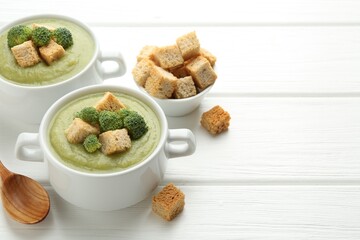 Tasty broccoli cream soup with croutons served on white wooden table, closeup. Space for text
