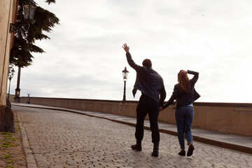 Fototapeta premium A couple strolls hand in hand along a charming, cobblestone street, joyfully waving at something delightful offscreen, exploring their city