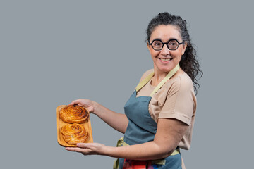 Smiling female baker holding delicious cinnamon buns