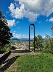 View from Castle Hill above Česká Kamenice, featuring a modern metal bell tower, sunny summer day, city and surrounding hills in the distance.
