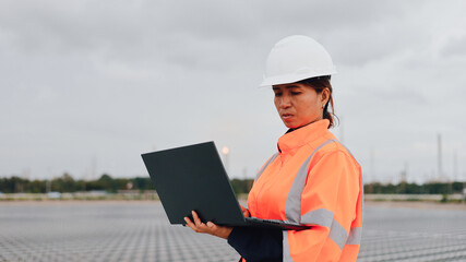 A construction worker in an orange safety jacket and white hard hat reviews information on a laptop...