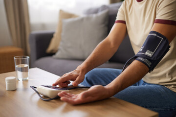 A person monitors their blood pressure while seated at a table in a comfortable living room,...