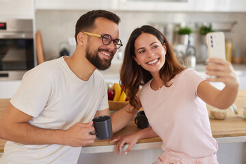 Two people enjoy morning time together in a bright kitchen. They smile happily as they take a selfie, capturing the start of their day filled with joy and connection.