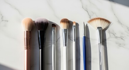Assortment of makeup brushes with varying sizes and shapes, neatly arranged on a white marble surface, showcasing beauty tools for cosmetic application
