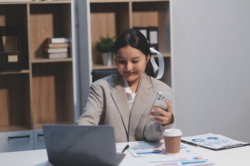 Positive asian young female accountant using a smartphone at her office desk. Woman relaxing on her mobile application.