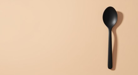 Minimalist black spoon casting a shadow on a peach background