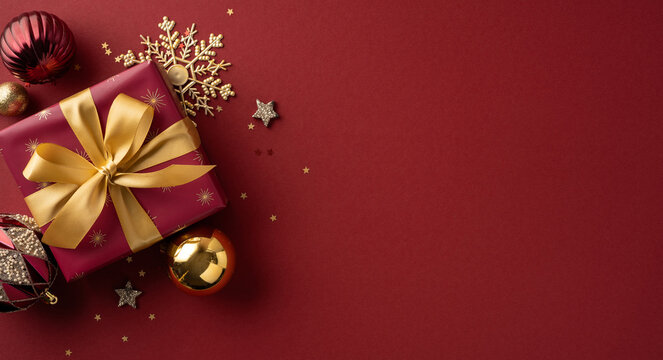 A festive scene featuring a burgundy gift box with a gold ribbon, gold ornaments, and a decorative snowflake against a rich red backdrop
