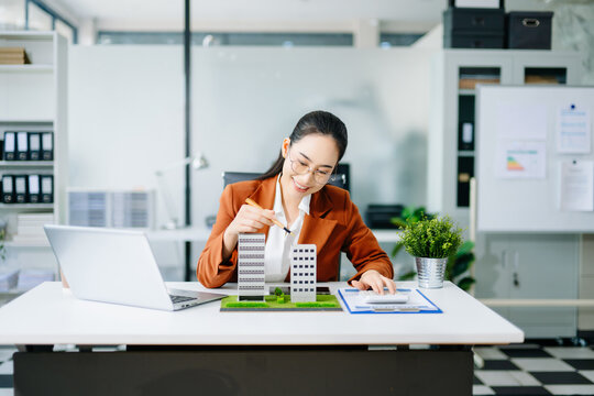 Confident businesswoman analyzing building models at office desk. Perfect for real estate, property investment, mortgage planning, and corporate finance themes. - Powered by Adobe