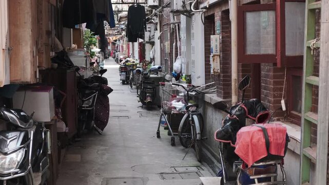 Narrow alley in China is densely packed with parked scooters, bicycles, and laundry hanging between old residential buildings