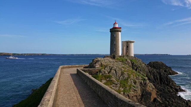 Scenic view of historic Petit Minou Lighthouse on rocky islet, stone tower, causeway, and blue sea with ferry, Brittany, France