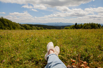 Fototapeta premium Close-up of sneakers and feet of a resting tourist lying on the grass in the middle of a picturesque field.