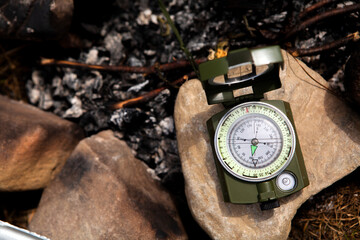 Green metal compass lying on the rock near the fireplace, concept of tourist equipment, finding the right direction of the path.