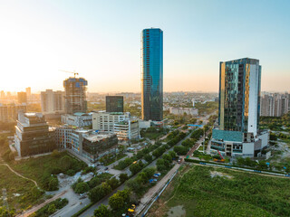 Aerial view of modern skyscrapers towering over verdant trees and manicured lawns on Golf Course Extension Road under a hazy sky, Gurugram, Haryana, India.