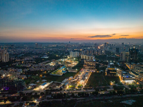 Aerial view of the city's illuminated skyline meeting the horizon, as twilight paints the sky with vibrant hues, Golf Course Extension Road, Gurugram, Haryana, India.
