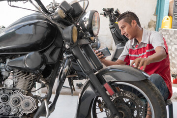 Mechanic man inspecting motorcycle using phone technology