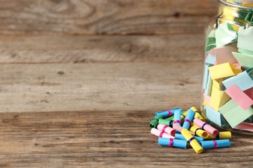 Colorful paper pieces in glass jar on wooden table, closeup. Space for text. Notes with messages