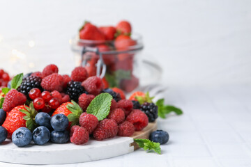 Different ripe berries and mint leaves on white tiled table, closeup. Space for text